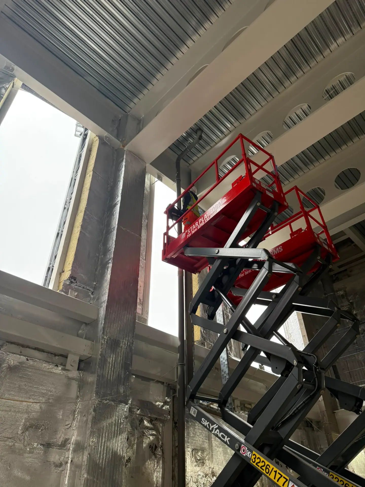 Delta Facades installer working from a Skyjack scissor lift to access a high-level facade interface